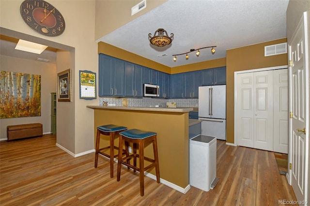 kitchen with blue cabinets, a kitchen bar, hardwood / wood-style flooring, kitchen peninsula, and high end white refrigerator