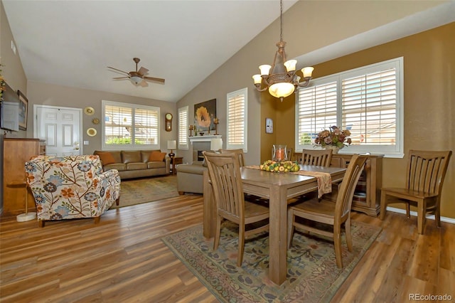 dining area featuring ceiling fan with notable chandelier, wood-type flooring, and lofted ceiling