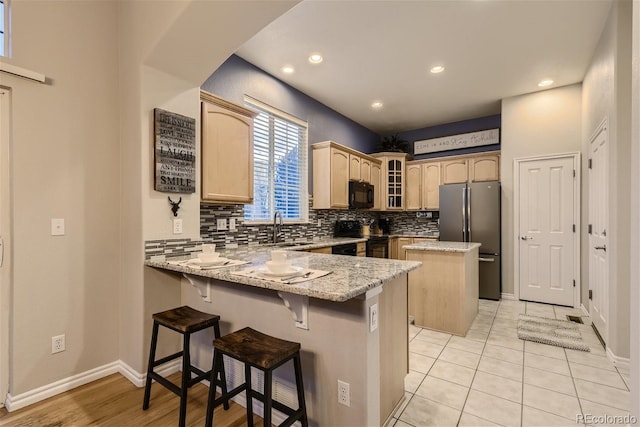 3120 Redhaven Way, Highlands Ranch, CO 80126 - kitchen with a peninsula, light stone countertops, glass insert cabinets, a center island, and black appliances