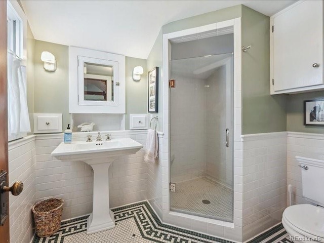 full bathroom featuring tile walls, toilet, a shower stall, wainscoting, and tile patterned floors