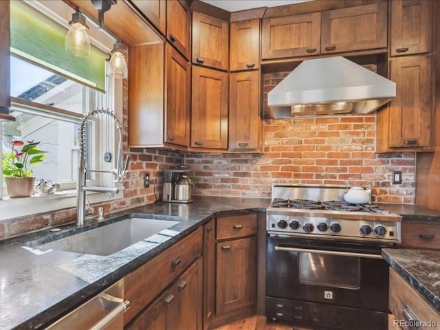 kitchen featuring stainless steel appliances, under cabinet range hood, brown cabinetry, and dark stone countertops