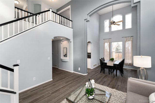 living room featuring a towering ceiling, ceiling fan, and dark wood-type flooring