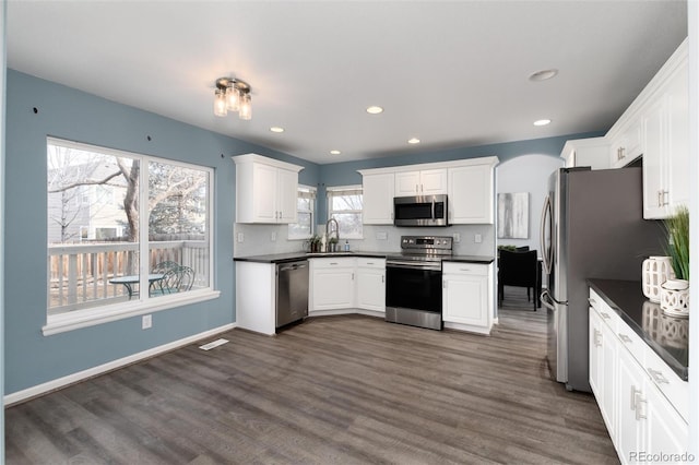 kitchen with dark hardwood / wood-style flooring, stainless steel appliances, white cabinetry, and tasteful backsplash