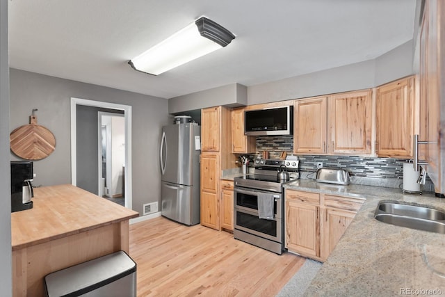 kitchen with appliances with stainless steel finishes, light brown cabinetry, light hardwood / wood-style floors, and backsplash