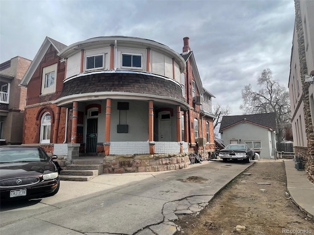 view of front facade with brick siding, a porch, and a shingled roof