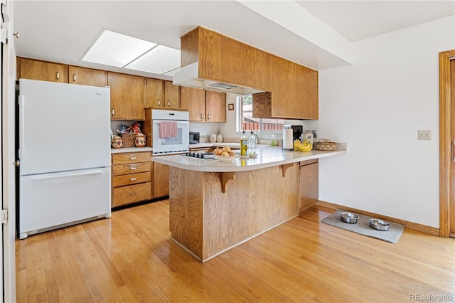 12522 W Virginia Ave, Lakewood, CO 80228 - kitchen with white appliances, light wood-style flooring, a peninsula, brown cabinetry, and light countertops