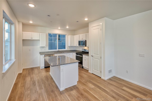 kitchen with a sink, a kitchen island, visible vents, appliances with stainless steel finishes, and light wood finished floors