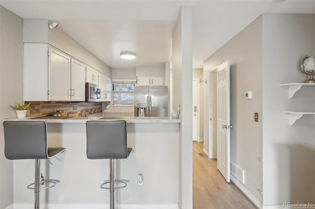 1818 S Quebec Way Unit 11-3, Denver, CO 80231 - kitchen featuring stainless steel appliances, a breakfast bar area, white cabinets, tasteful backsplash, and a peninsula
