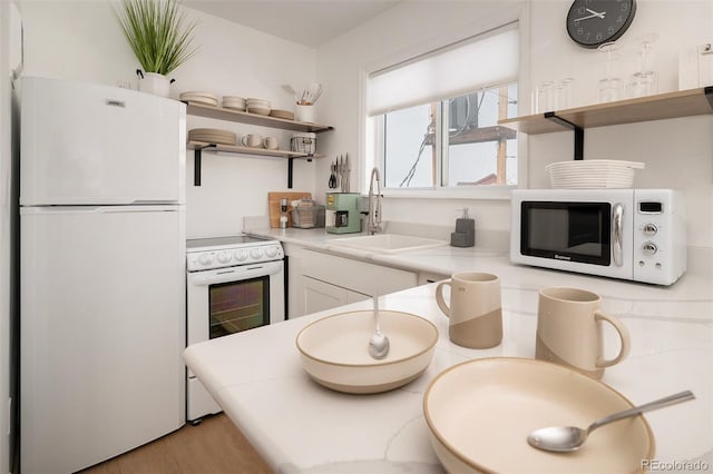 kitchen with white cabinets, sink, white appliances, and light hardwood / wood-style flooring