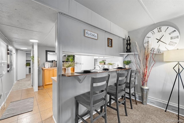 kitchen with a kitchen breakfast bar, light colored carpet, light brown cabinetry, and a textured ceiling