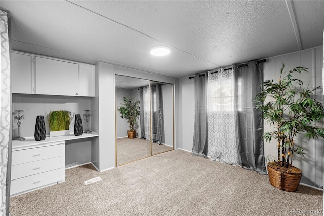 carpeted bedroom with a textured ceiling, built in desk, and a closet