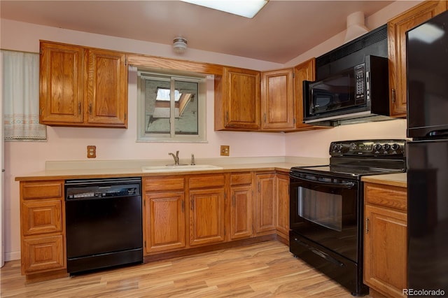 kitchen featuring brown cabinets, a sink, black appliances, light countertops, and light wood-type flooring