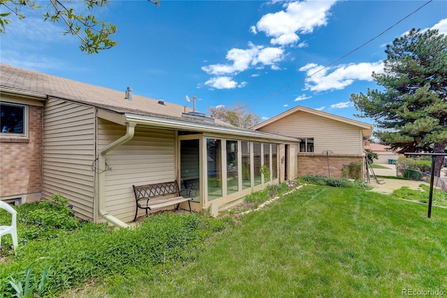 rear view of property featuring a yard, fence, brick siding, and a sunroom