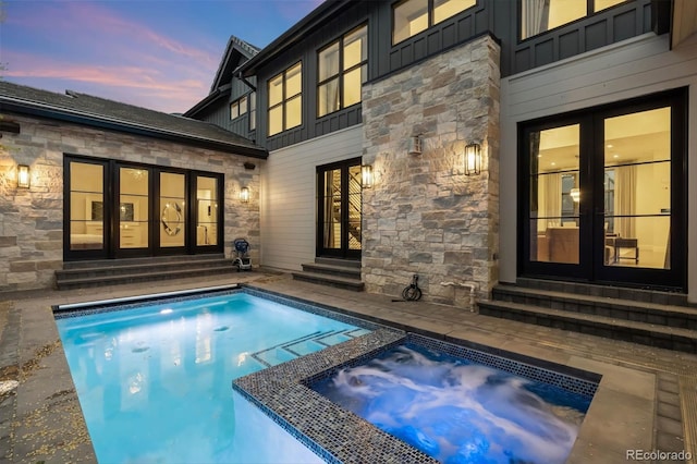 rear view of house featuring a pool with connected hot tub, stone siding, board and batten siding, entry steps, and french doors