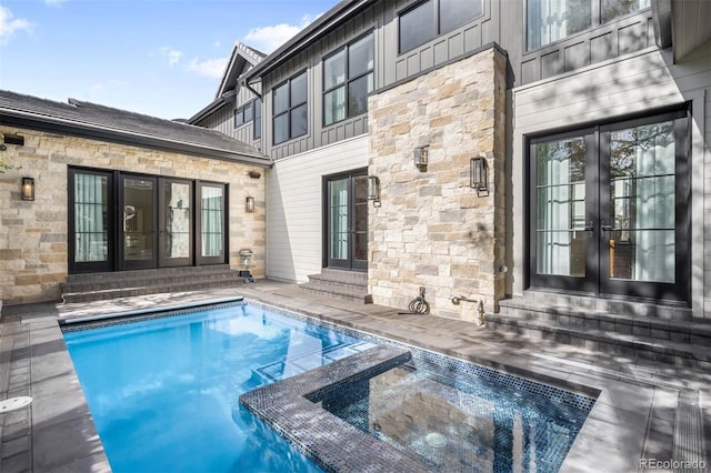 exterior space featuring stone siding, french doors, board and batten siding, entry steps, and a pool with connected hot tub