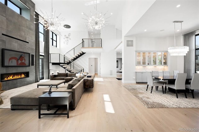 living area with stairway, visible vents, a notable chandelier, and a towering ceiling
