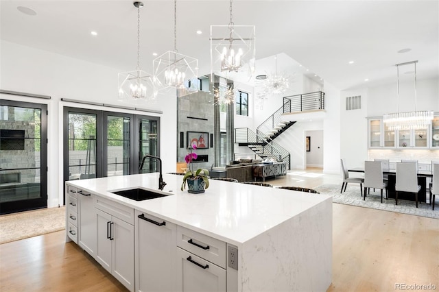 kitchen featuring an inviting chandelier, a sink, light wood finished floors, open floor plan, and a towering ceiling