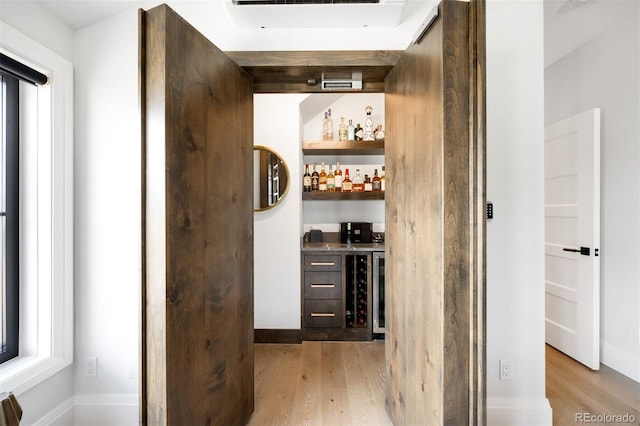 bar with a bar, light wood finished floors, wine cooler, and baseboards