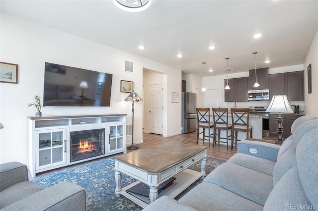 living area with recessed lighting, baseboards, visible vents, a glass covered fireplace, and wood finished floors