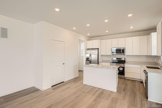 kitchen featuring stainless steel appliances, white cabinetry, a center island, and sink