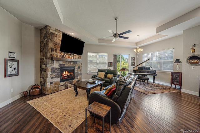 living room with a tray ceiling, dark wood finished floors, plenty of natural light, and a stone fireplace