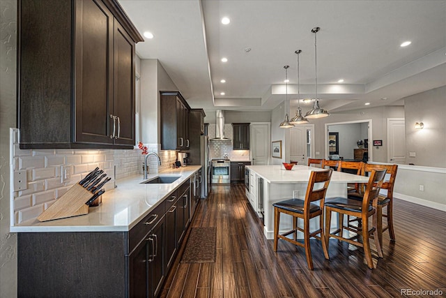 kitchen with a spacious island, wall chimney exhaust hood, light countertops, and a sink