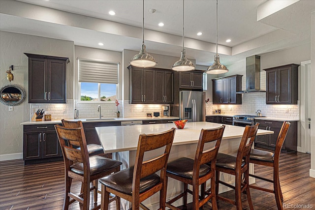 kitchen with decorative backsplash, wall chimney exhaust hood, a center island, stainless steel appliances, and dark hardwood / wood-style flooring