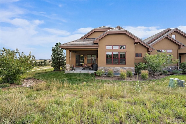 rear view of house featuring stone siding, a patio, and stucco siding