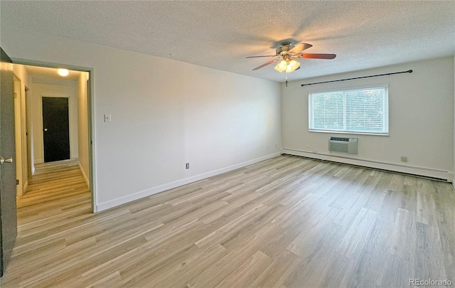 empty room with ceiling fan, light hardwood / wood-style floors, a textured ceiling, a baseboard heating unit, and a wall mounted air conditioner