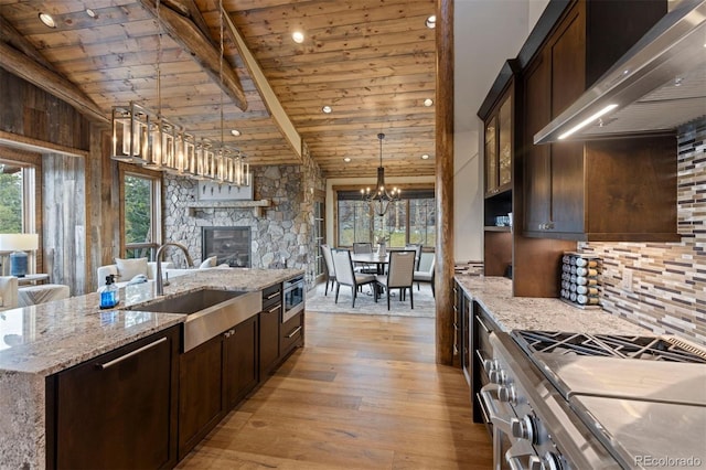 kitchen featuring wall chimney range hood, vaulted ceiling with beams, sink, light wood-type flooring, and appliances with stainless steel finishes