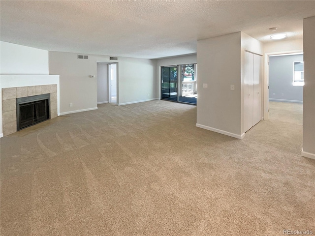 unfurnished living room with light carpet, a tiled fireplace, and a textured ceiling