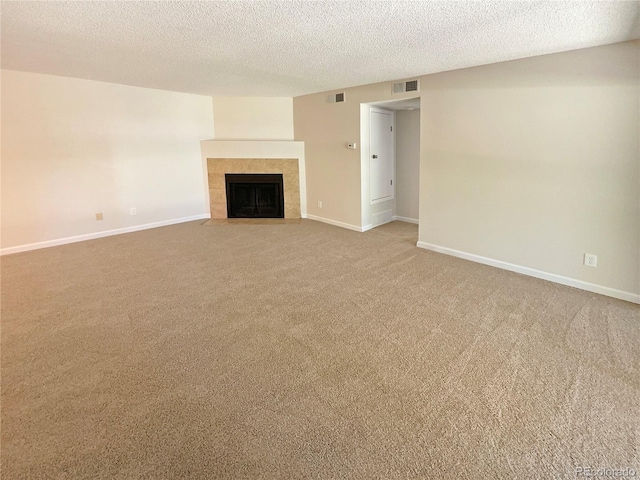 unfurnished living room with a tiled fireplace, a textured ceiling, and carpet floors