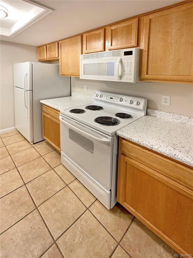 kitchen with white appliances, light stone counters, and light tile patterned floors