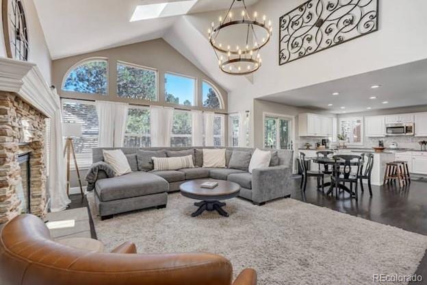 living room featuring a chandelier, a stone fireplace, a skylight, high vaulted ceiling, and dark wood-style floors