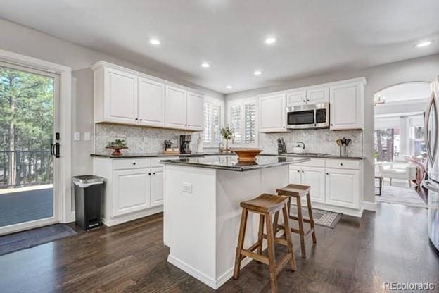 kitchen featuring stainless steel microwave, dark wood-style floors, dark countertops, a center island, and recessed lighting