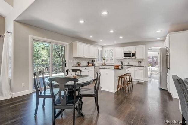 dining room featuring arched walkways, dark wood-style floors, recessed lighting, and baseboards