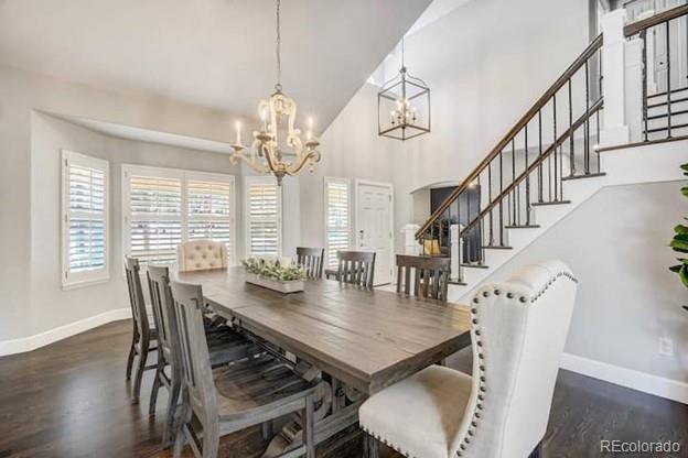 dining space with baseboards, a chandelier, stairs, wood finished floors, and high vaulted ceiling