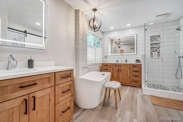 bathroom with a stall shower, wood finished floors, two vanities, a chandelier, and a soaking tub