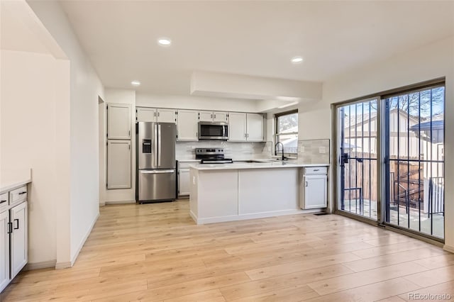 kitchen featuring kitchen peninsula, stainless steel appliances, light wood-type flooring, backsplash, and white cabinetry