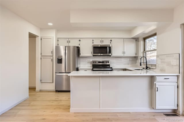 kitchen with stainless steel appliances, sink, light hardwood / wood-style flooring, white cabinetry, and backsplash