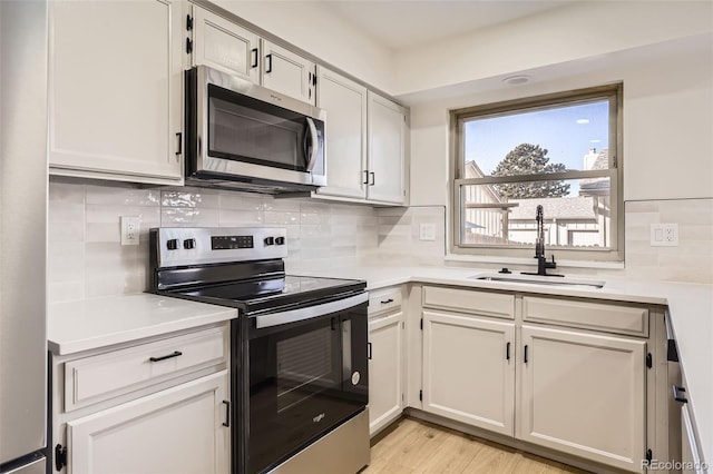 kitchen featuring appliances with stainless steel finishes, white cabinetry, light hardwood / wood-style flooring, and sink