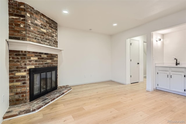 unfurnished living room featuring a fireplace, light wood-type flooring, and sink