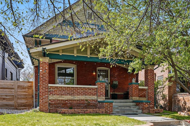 view of front of house featuring a porch, brick siding, fence, and a front lawn