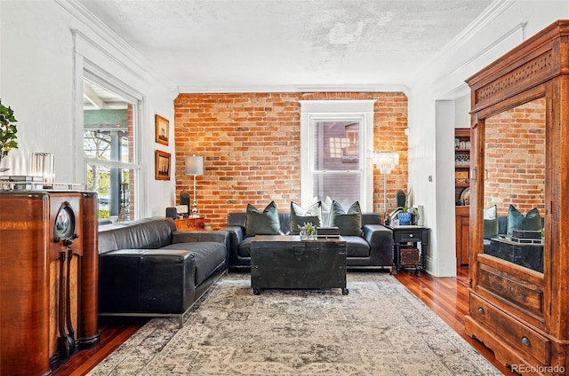 living room featuring brick wall, a textured ceiling, ornamental molding, and wood finished floors