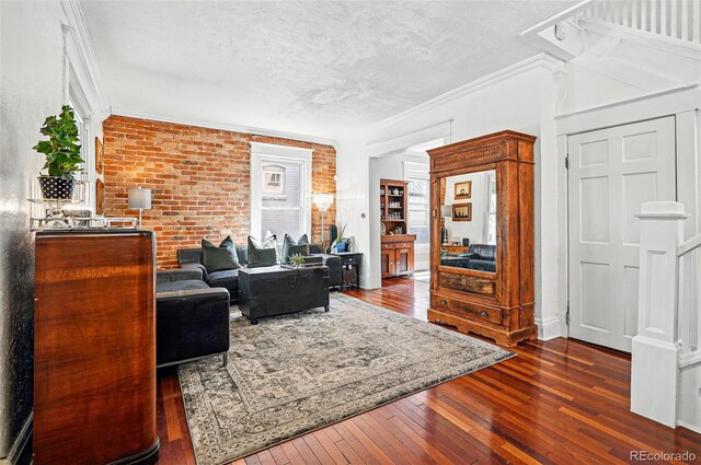 living area featuring crown molding, a textured ceiling, hardwood / wood-style flooring, and brick wall