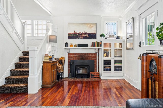 living area with a textured ceiling, hardwood / wood-style flooring, baseboards, ornamental molding, and stairs