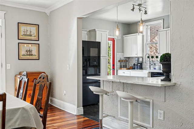 kitchen with visible vents, wood finished floors, fridge, a breakfast bar area, and white cabinetry