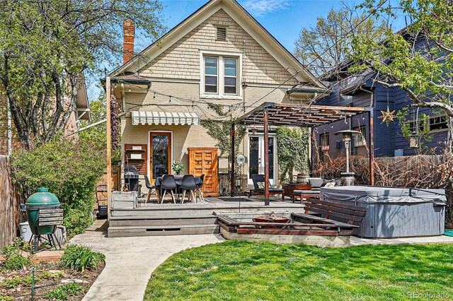 back of house featuring a hot tub, a deck, a pergola, and a lawn