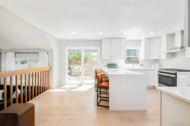 16438 E Prentice Cir, Centennial, CO 80015 - kitchen with stainless steel gas range, wall chimney exhaust hood, a breakfast bar area, healthy amount of natural light, and recessed lighting