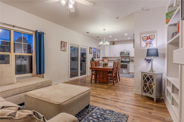 living room with ceiling fan with notable chandelier and light hardwood / wood-style flooring